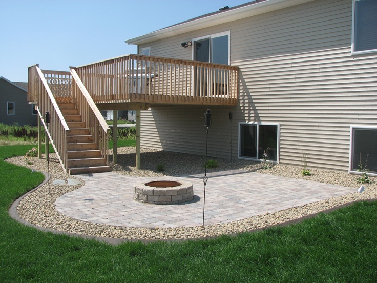 a patio with steps leading up to a deck and fire pit in the back yard