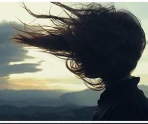 a woman with her hair blowing in the wind on top of a mountain at sunset