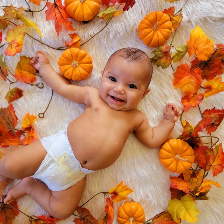 a baby in diapers is laying on the floor surrounded by pumpkins and leaves