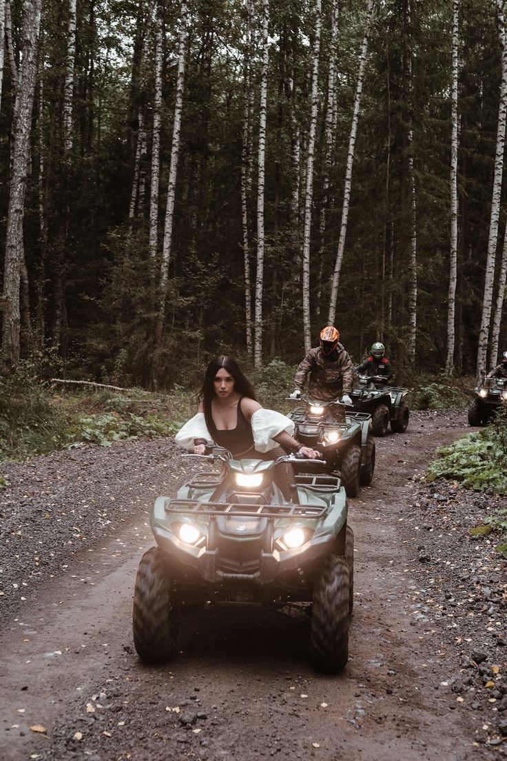 three people riding four wheelers in the woods