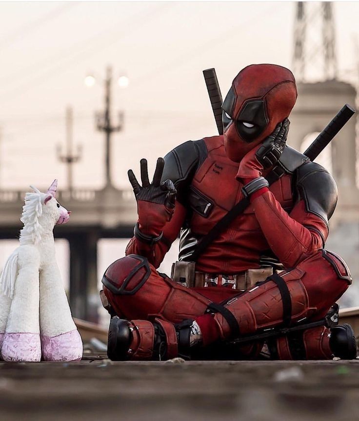 a deadpool sitting on the ground next to a toy llama and a stuffed animal