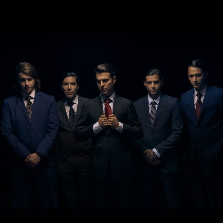 a group of men standing next to each other wearing suits and ties in front of a dark background