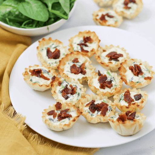 small appetizers on a white plate next to a bowl of spinach leaves