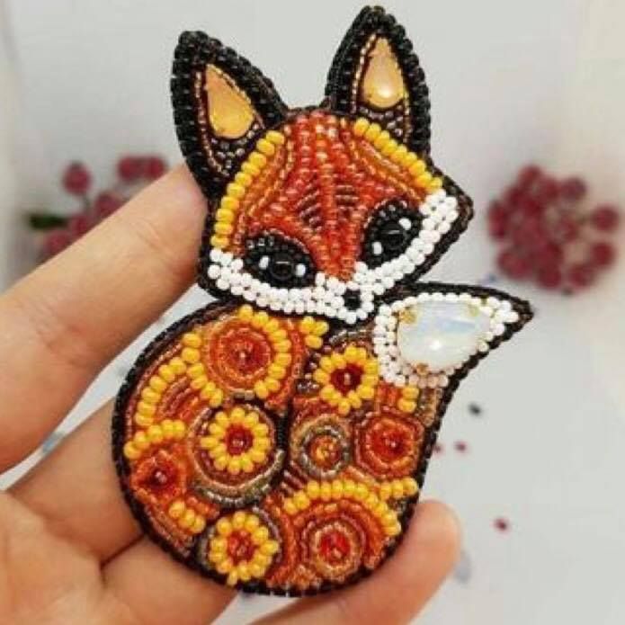 a hand holding a small beaded fox brooch