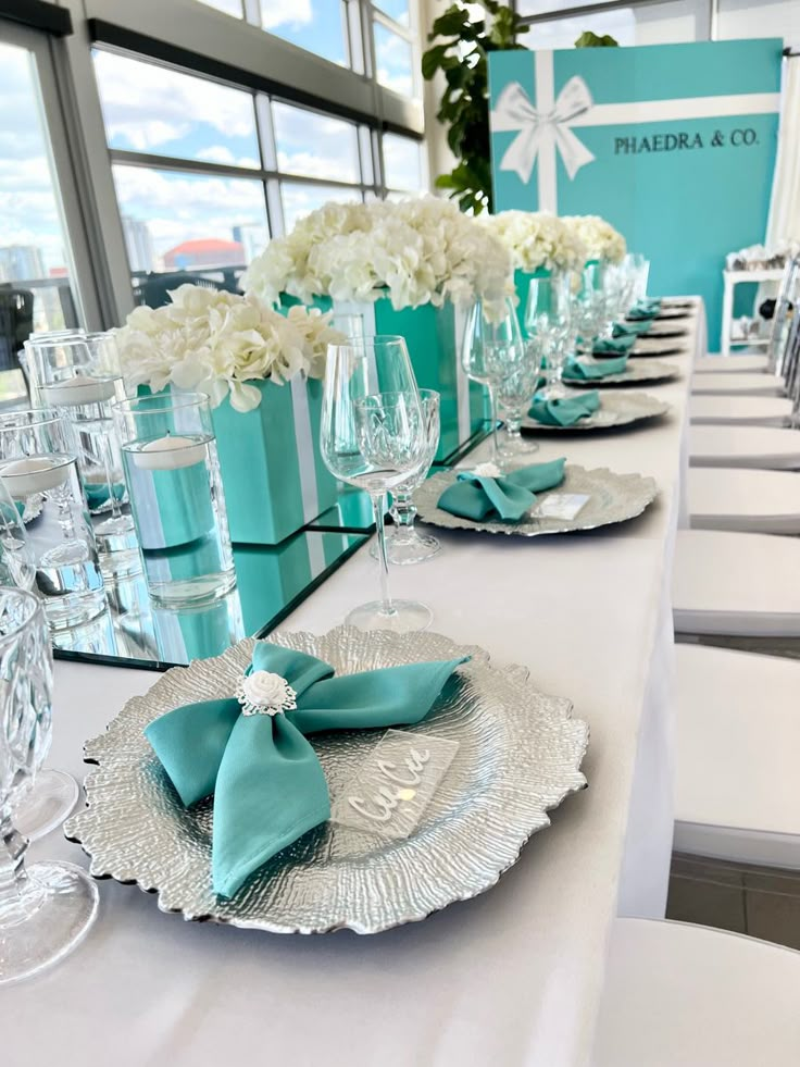 the table is set with white and aqua colored napkins, wine glasses, and silverware