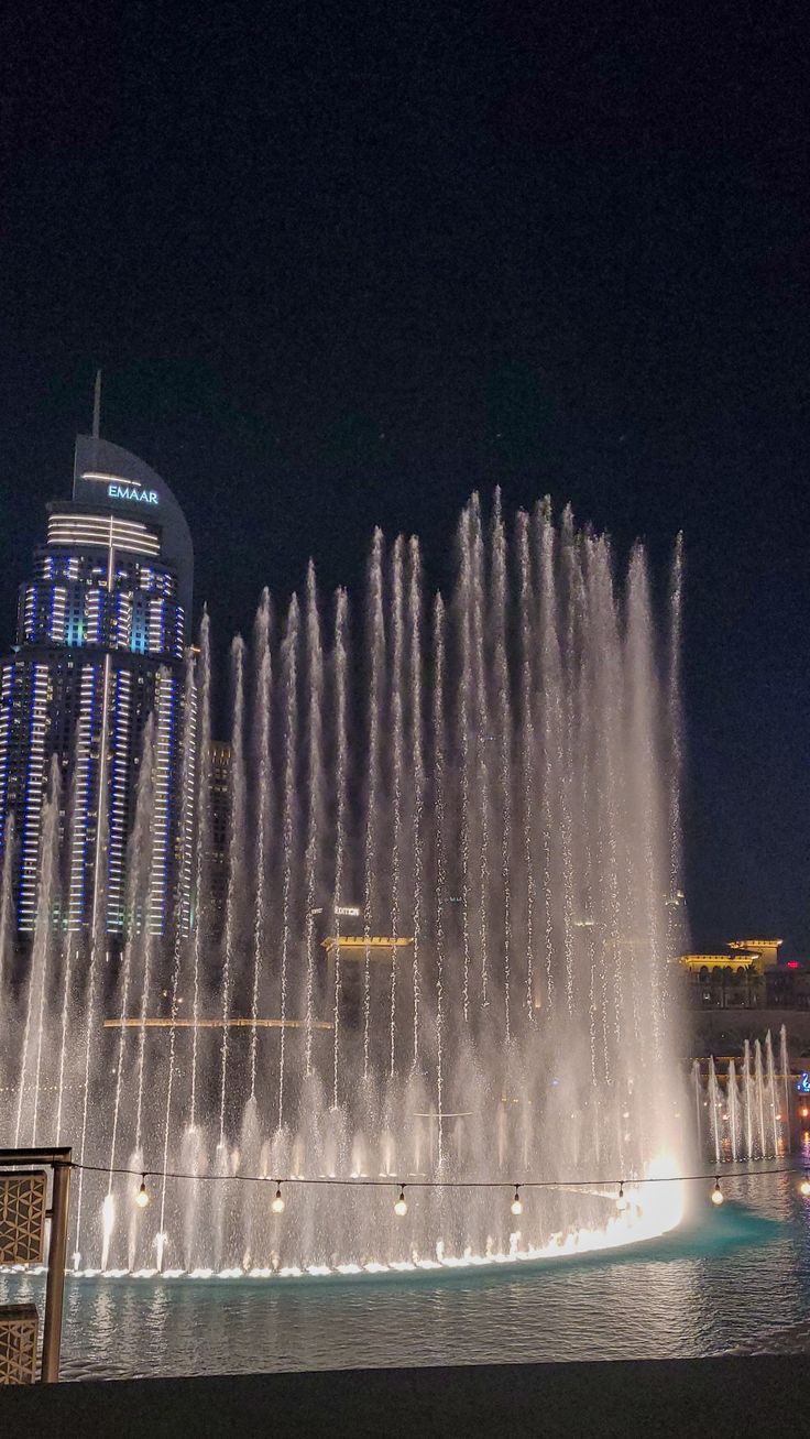 a large fountain is in the middle of a city square at night with lights on it