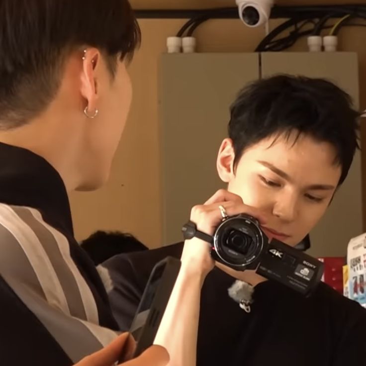 a man holding a camera up to his face while another person holds the camera in front of him