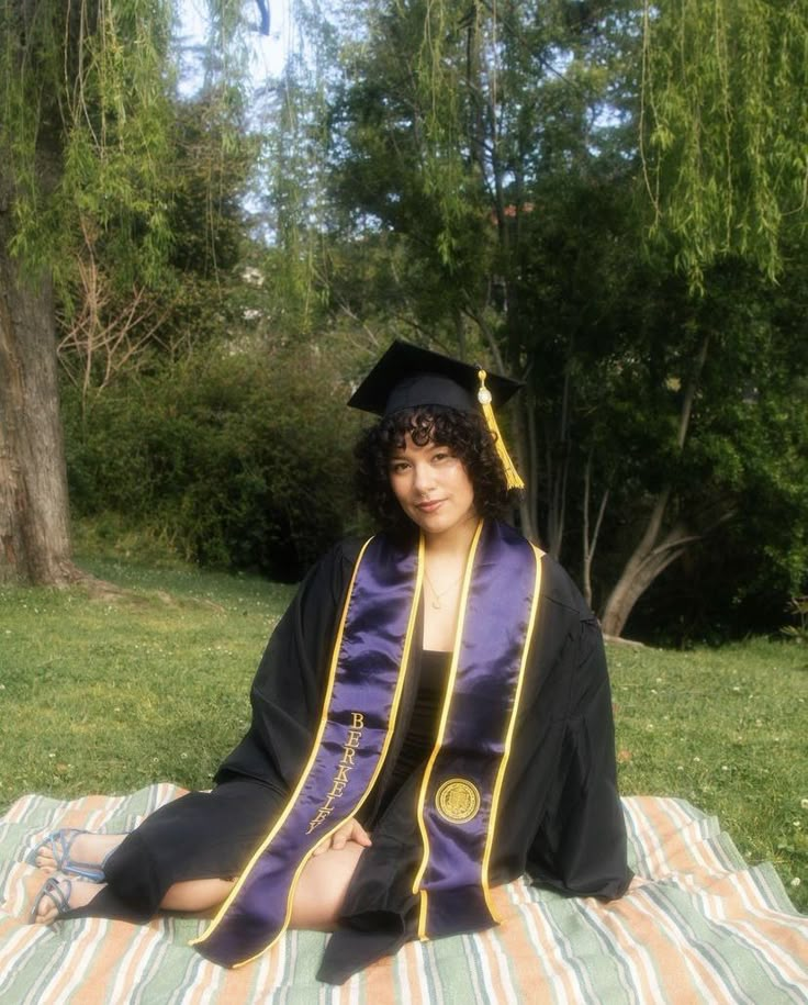 a woman sitting on top of a blanket wearing a graduation gown