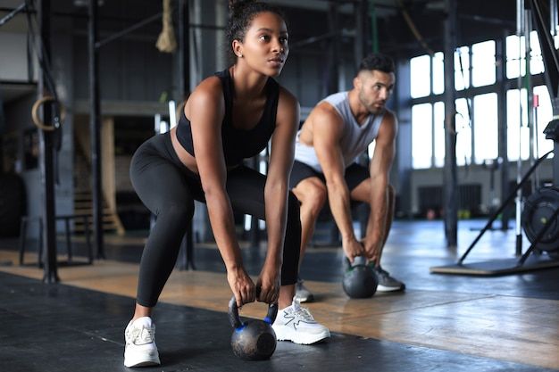 two people doing squats with kettles in a crossfit gym area, one holding a medicine ball