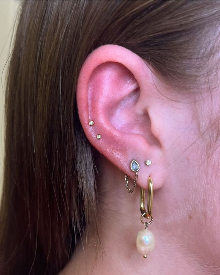 a close up of a person's ear wearing gold earrings and pearls on them