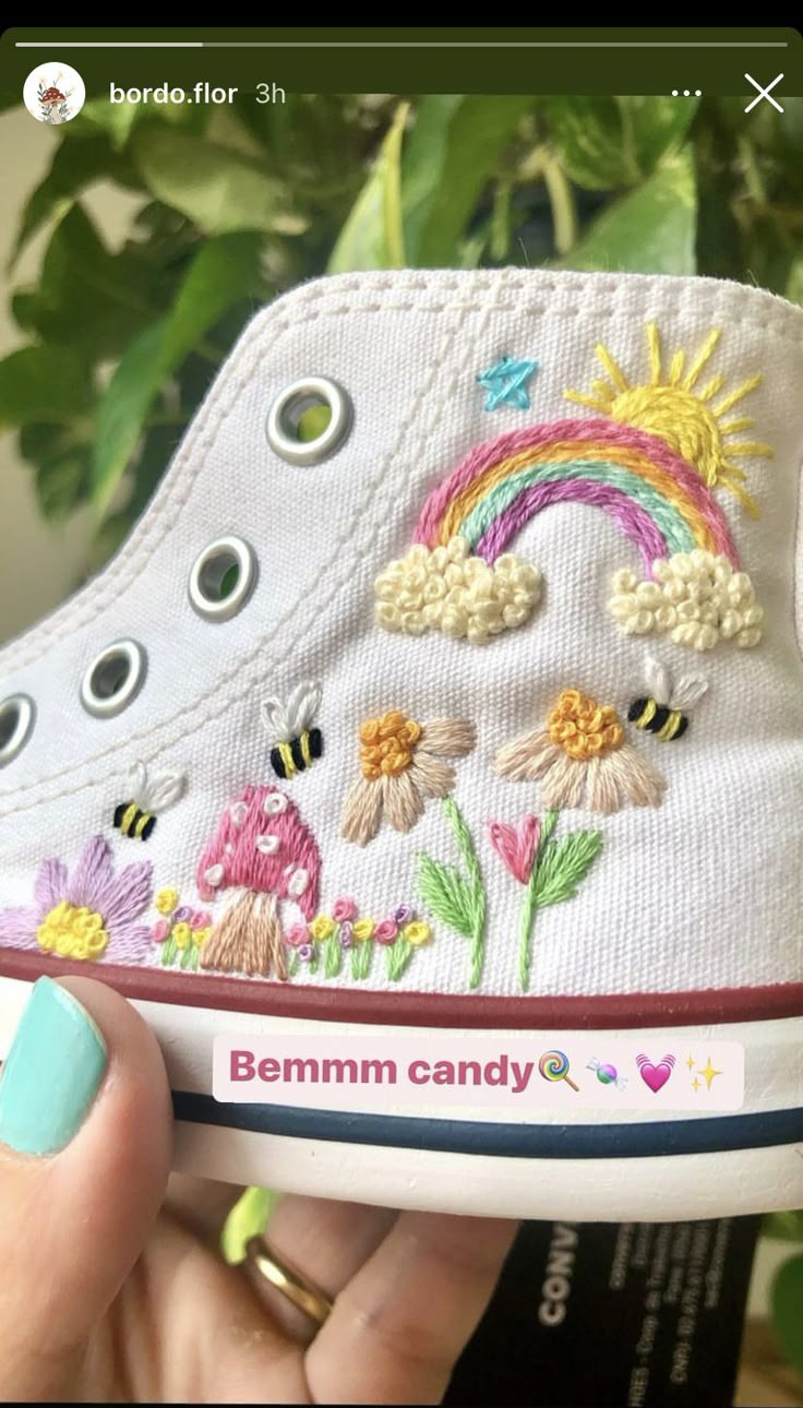 someone is holding up their white shoes with embroidered flowers and rainbows on the side