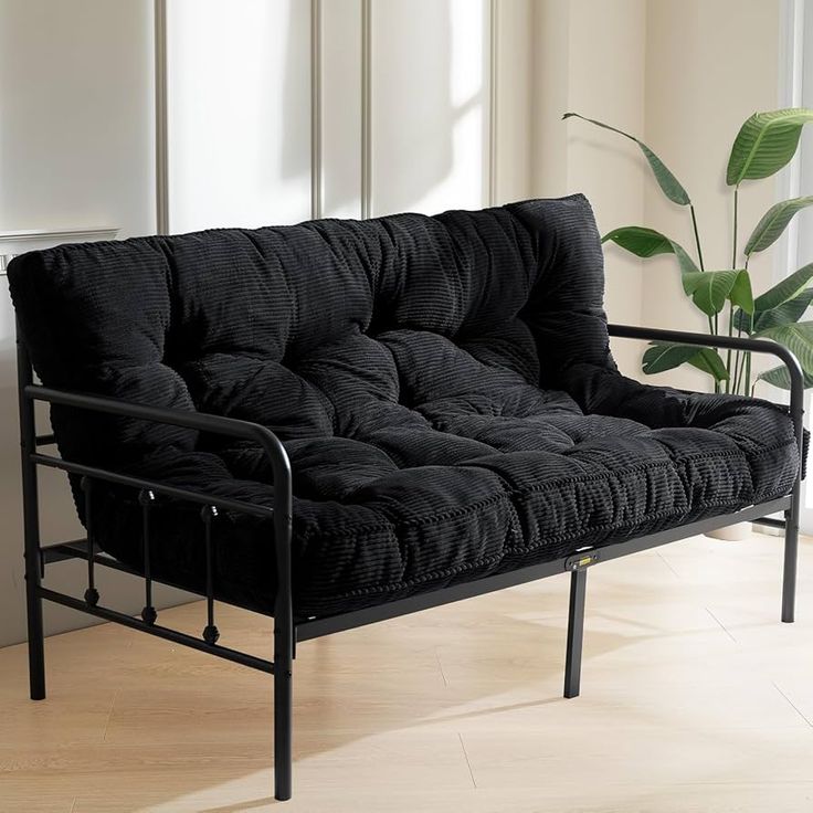 a black futon sofa sitting on top of a hard wood floor next to a potted plant