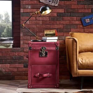 a red trunk sitting in front of a brick wall next to a chair and lamp