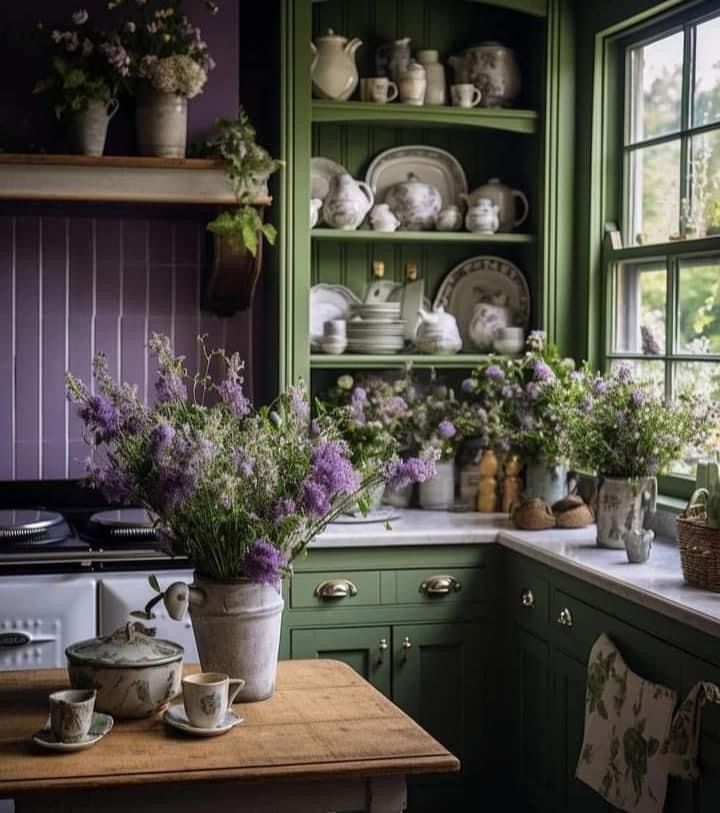 a kitchen filled with lots of green cupboards and purple flowers on the counter top