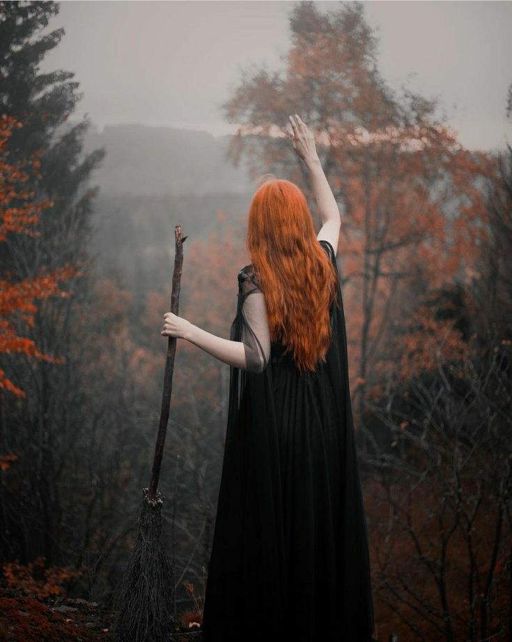 a woman with long red hair is holding a broom in the air while standing on a hill