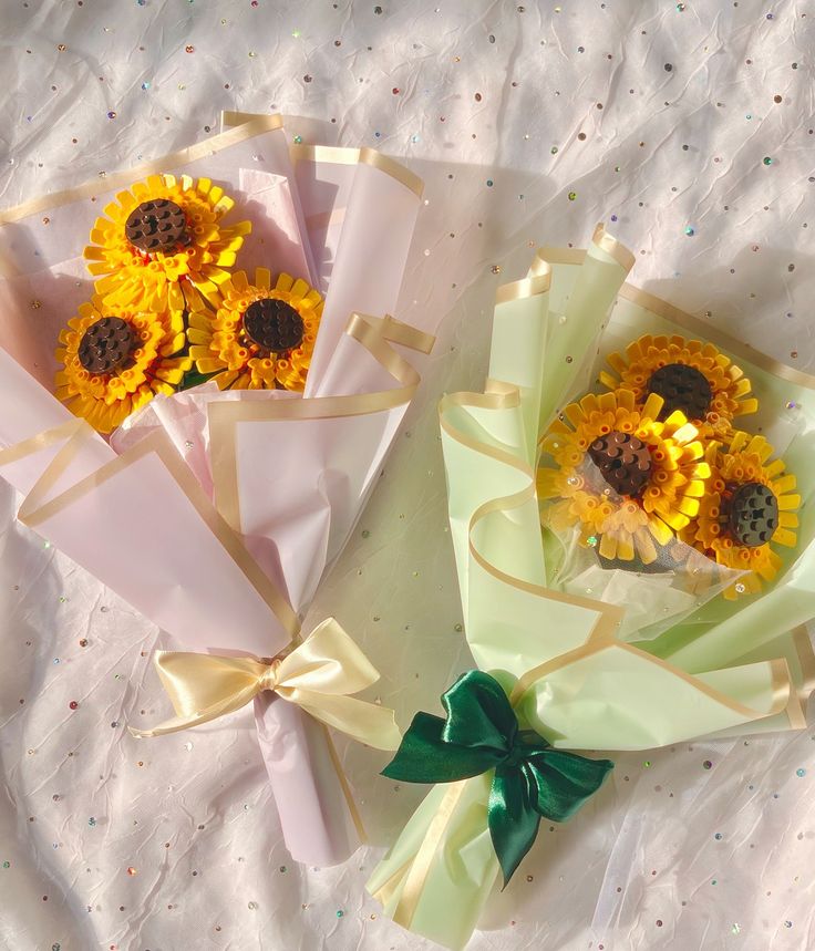 two sunflowers are wrapped in pink paper and tied with green ribbons on a bed