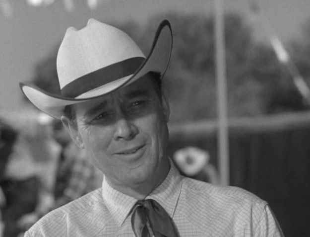 a man wearing a hat and tie with other people in the back ground behind him