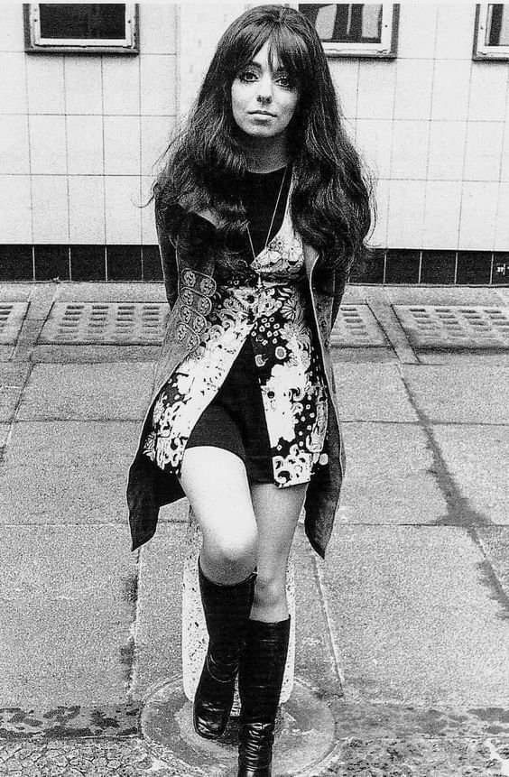 black and white photograph of a woman with long hair in high boots standing on the sidewalk