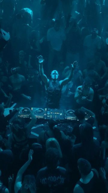 a dj mixing in front of a large group of people at a concert with their hands up