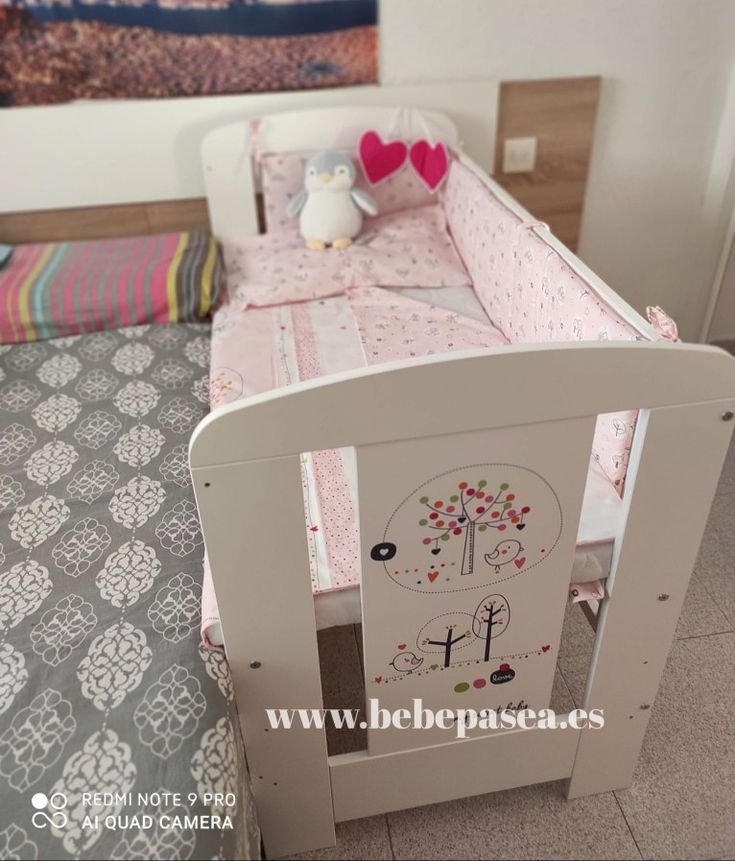 a baby crib with pink and white bedding on top of it, next to a small teddy bear