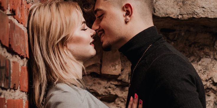 a man and woman standing next to each other near a brick wall with their faces close together