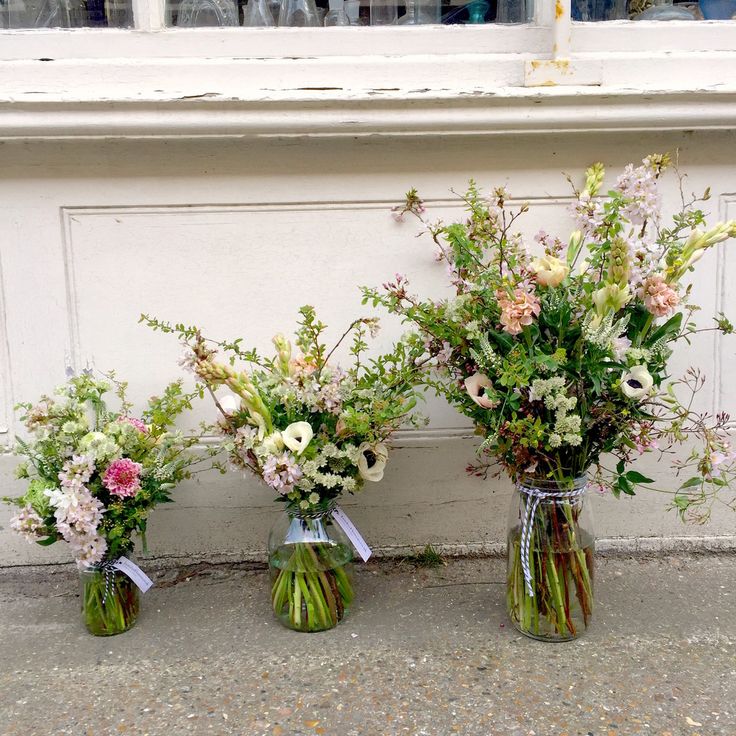 three vases filled with different types of flowers on the ground next to a wall