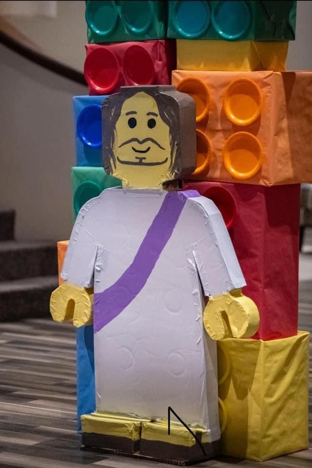 a lego man is standing in front of some colorful building blocks and holding a purple bag