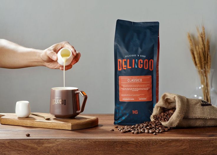 a person pouring coffee into a cup on top of a wooden table next to a bag of coffee beans