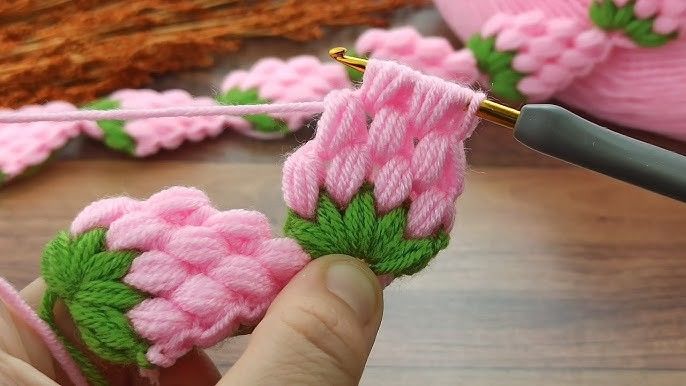 someone is knitting pink flowers with green leaves