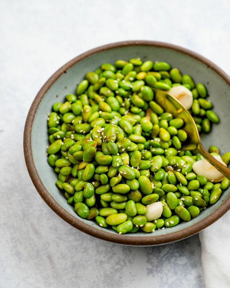 a bowl filled with green beans on top of a white table cloth next to a wooden spoon