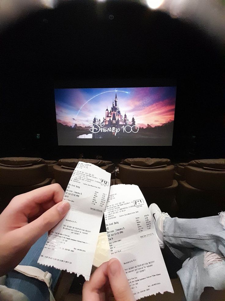 someone holding two tickets in front of a movie screen with the disney logo on it