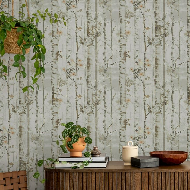 a table with books, plant and vase on it in front of a wallpapered background