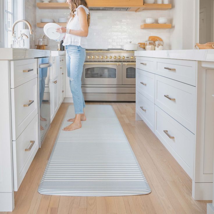 a woman standing in a kitchen holding a white plate and looking at the counter top