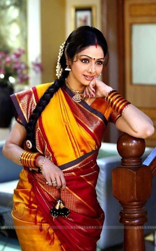 a woman in a yellow and red sari posing on a wooden railing with her hand under her chin