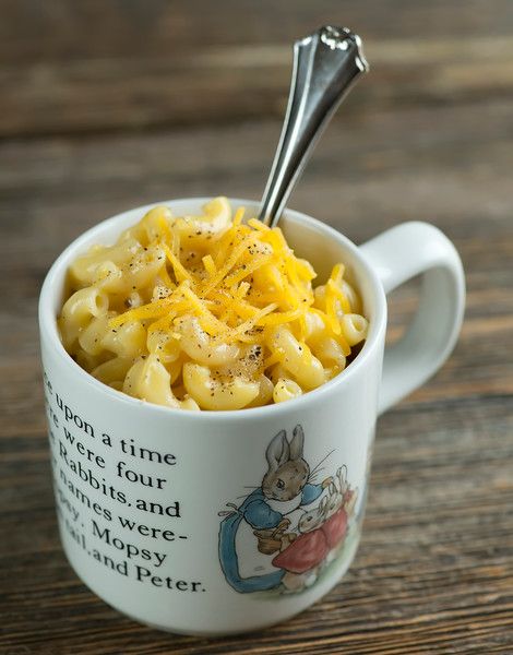 a cup filled with macaroni and cheese on top of a wooden table