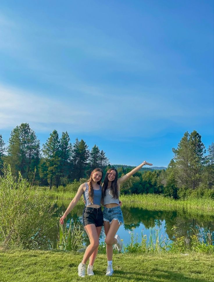 two young women standing next to each other in front of a lake