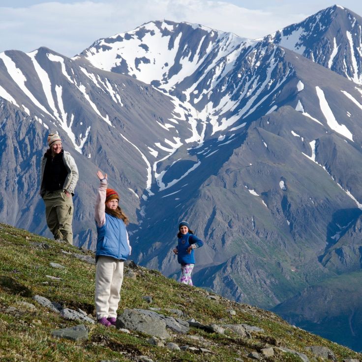 two children and an adult standing on top of a hill with snow covered mountains in the background