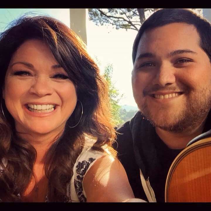 a man and woman smile as they pose for the camera with an acoustic guitar in front of them