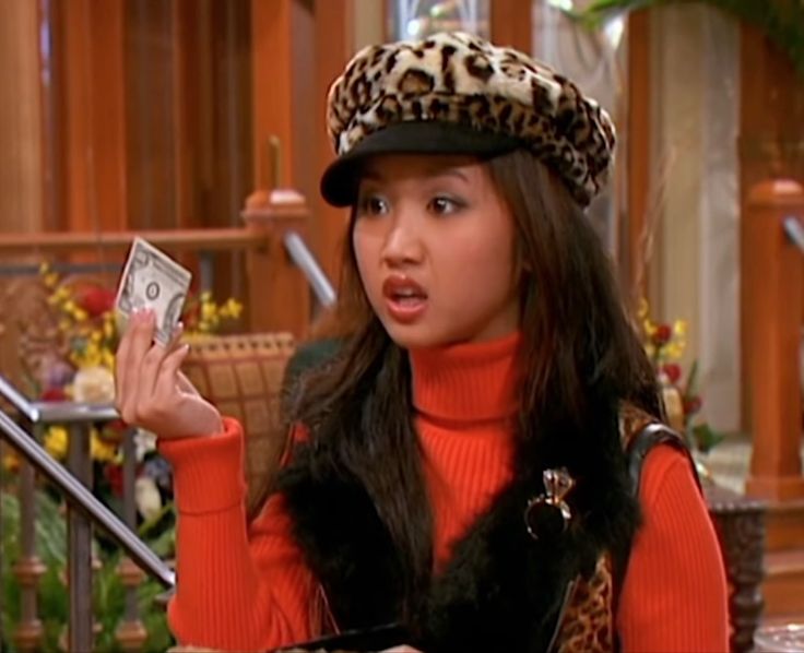 a woman in a leopard print hat holding up a money bill and looking at the camera