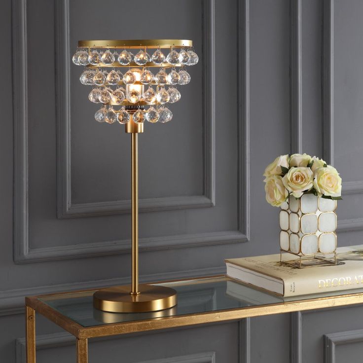 a gold table lamp with crystal balls on it next to a book and flower vase