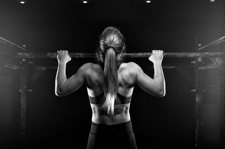 a woman with long hair standing in front of a gym rack holding a barbell