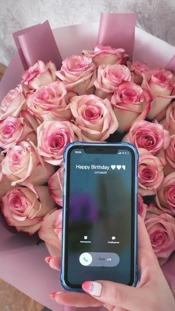 a person holding a cell phone in front of a bouquet of roses