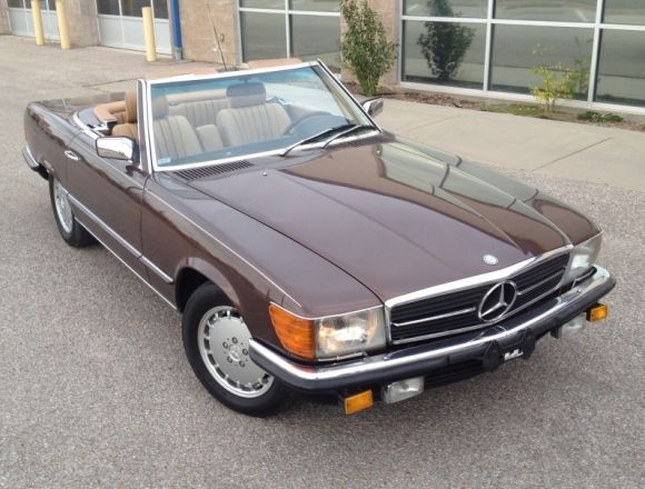 a brown mercedes benz is parked in front of a building with large windows and doors