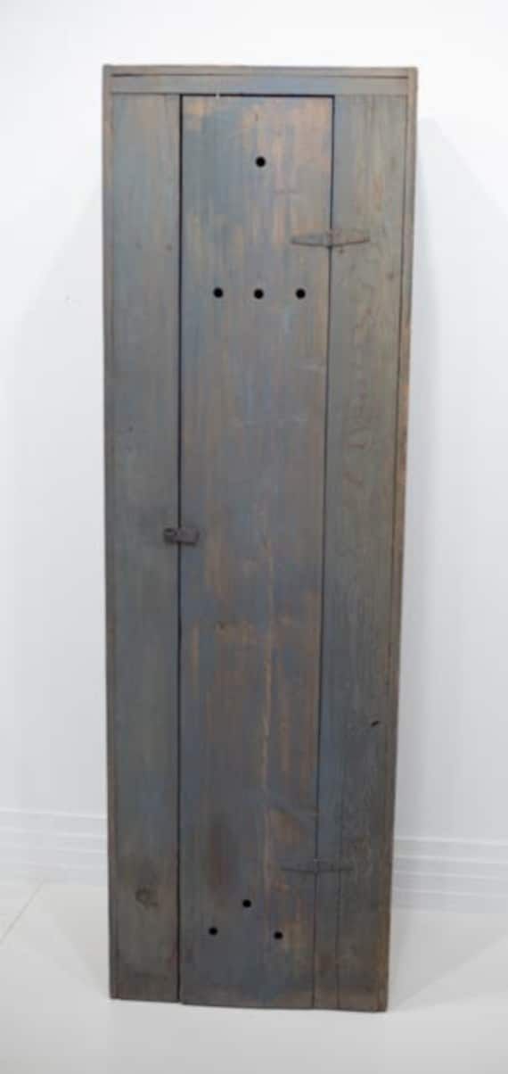 an old wooden cabinet with holes in the bottom and two doors on one side, against a white wall