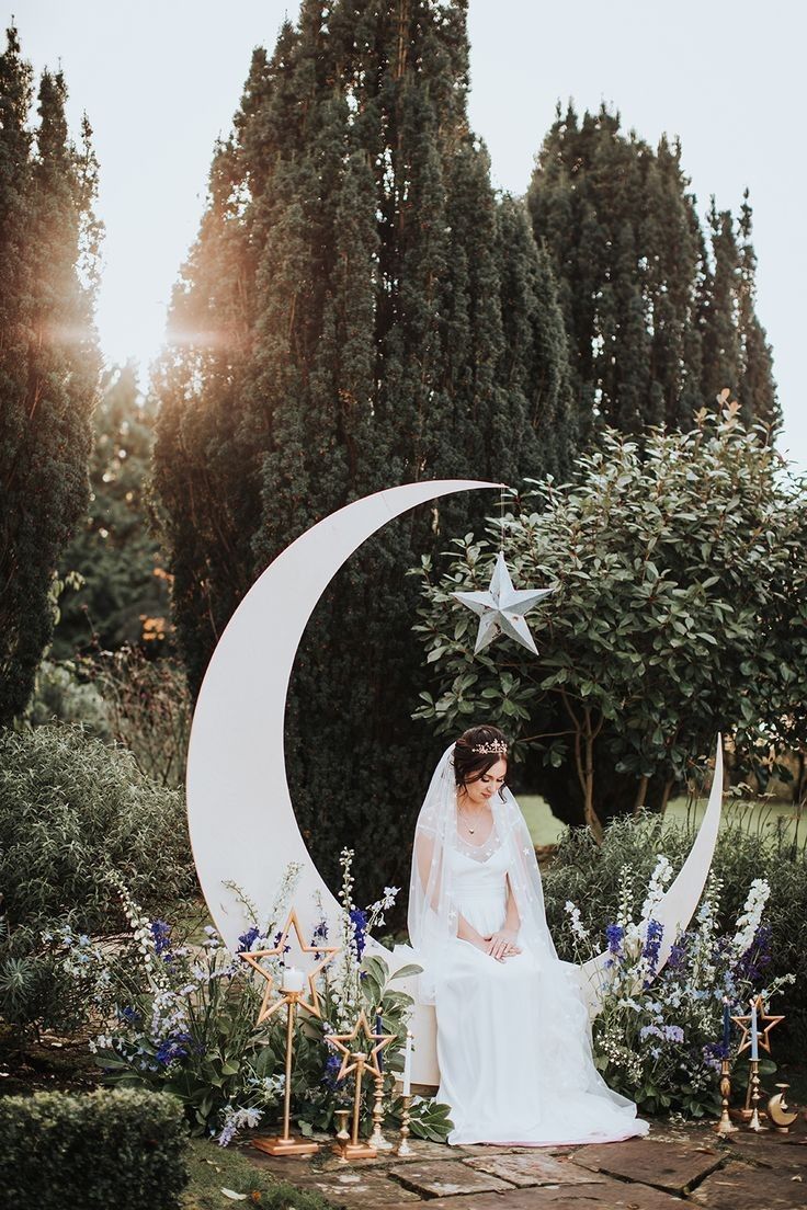 a bride sitting on the moon surrounded by flowers and greenery in front of trees