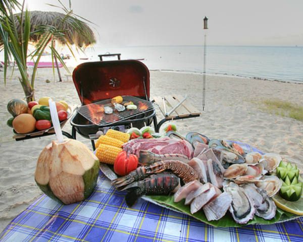 a table with food on it and an open grill in the sand at the beach