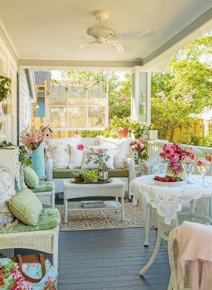 the porch is decorated with white wicker furniture and flowers in vases on tables