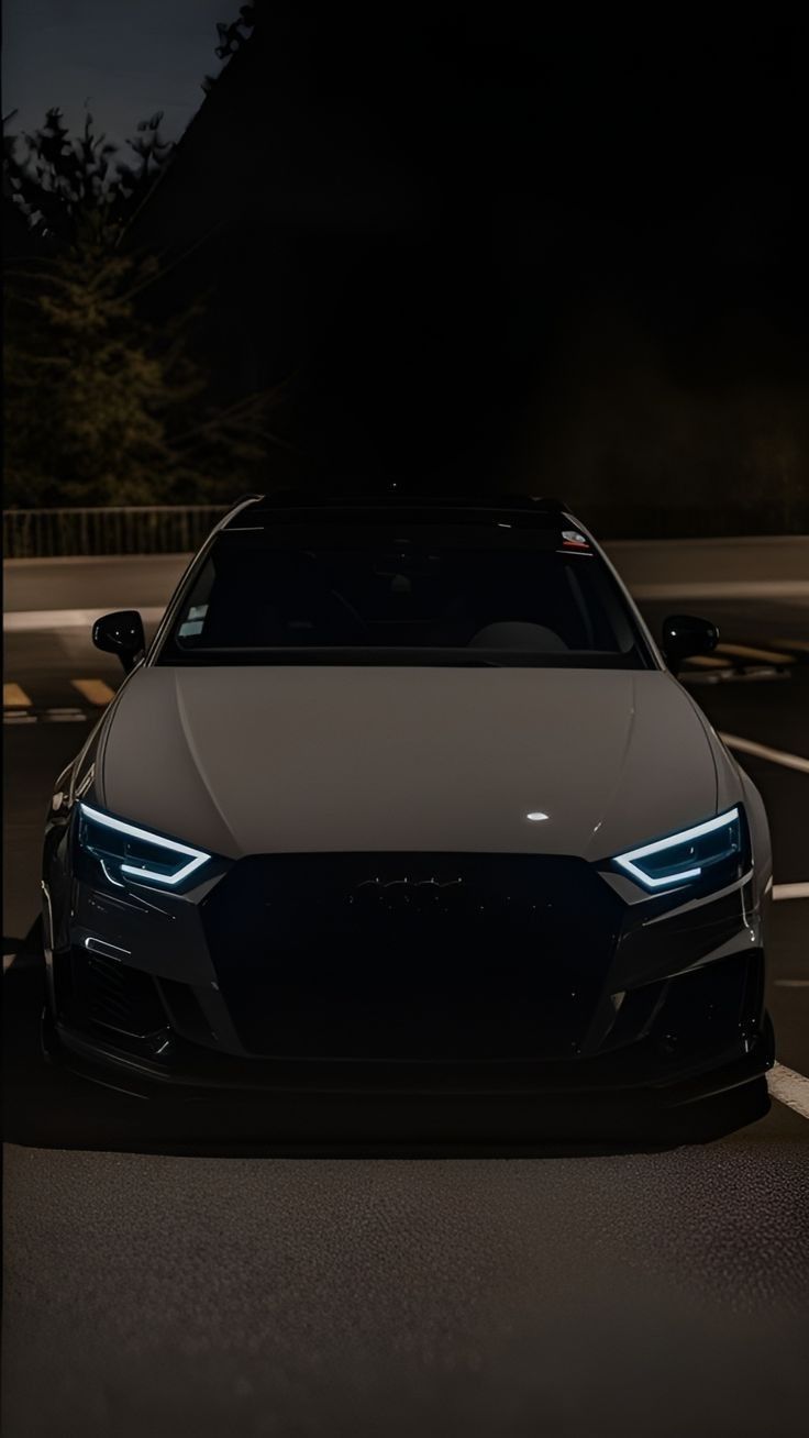 the front end of a black and white sports car at night with its lights on