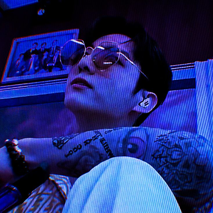 a man with tattoos on his arm and glasses laying down next to a tv screen