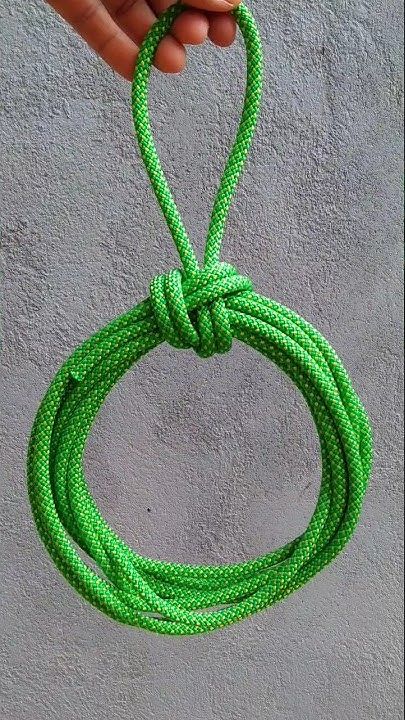 a hand holding a green rope on top of a cement wall with the end in the air